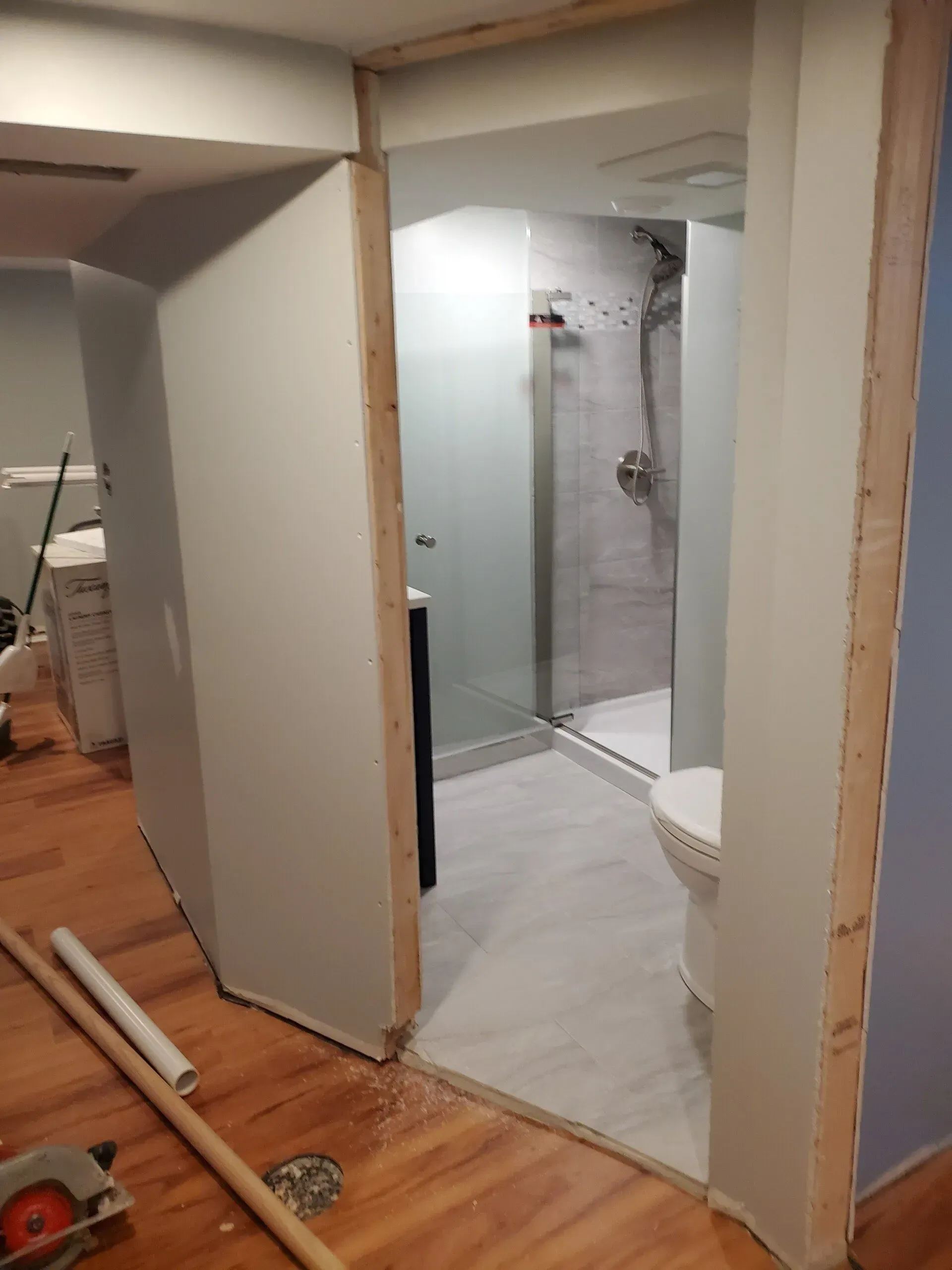 Bathroom under construction with new shower, toilet, and vanity visible through a doorway.