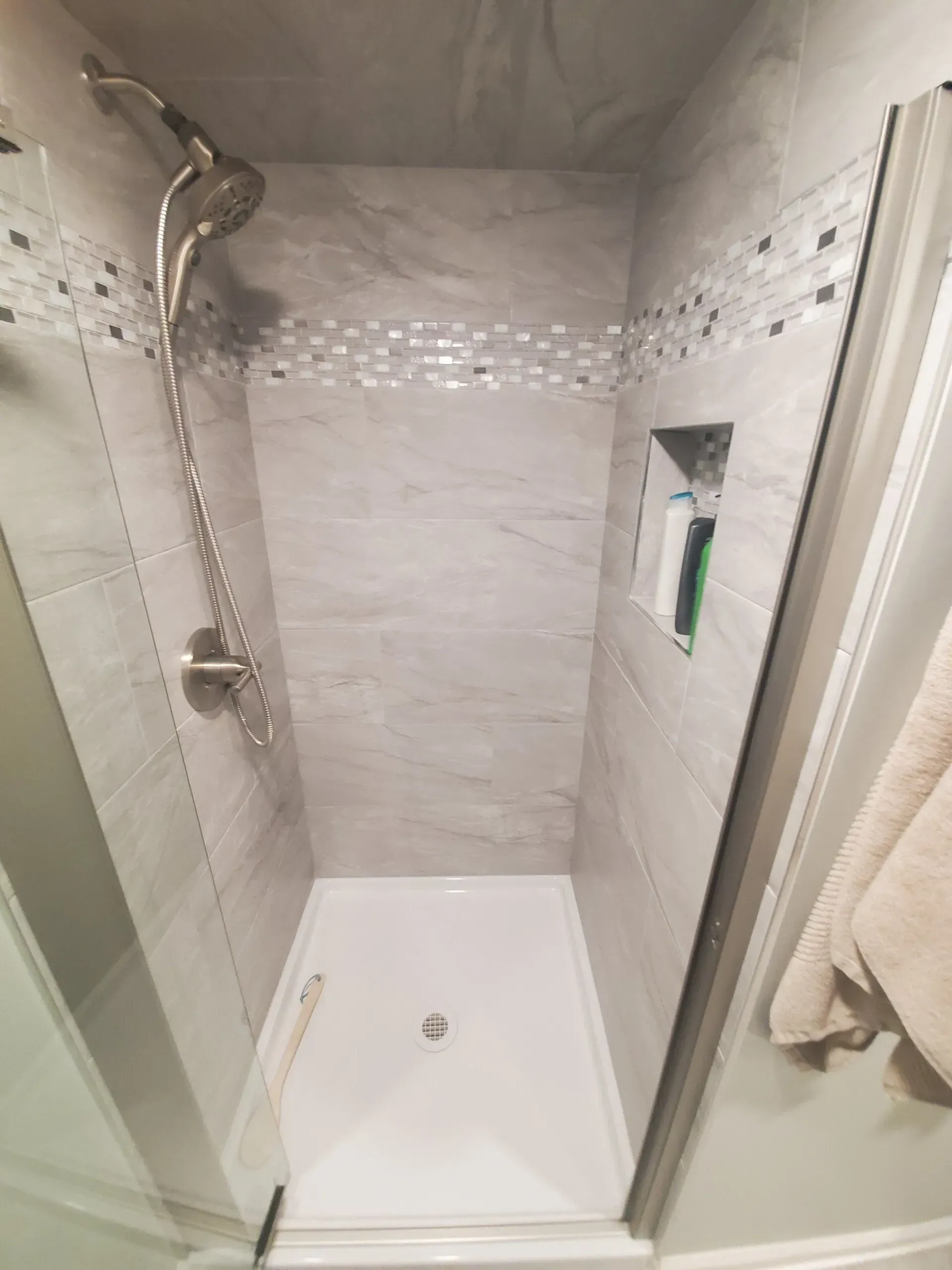 Shower with gray tiled walls, decorative strip, and built-in shelf.