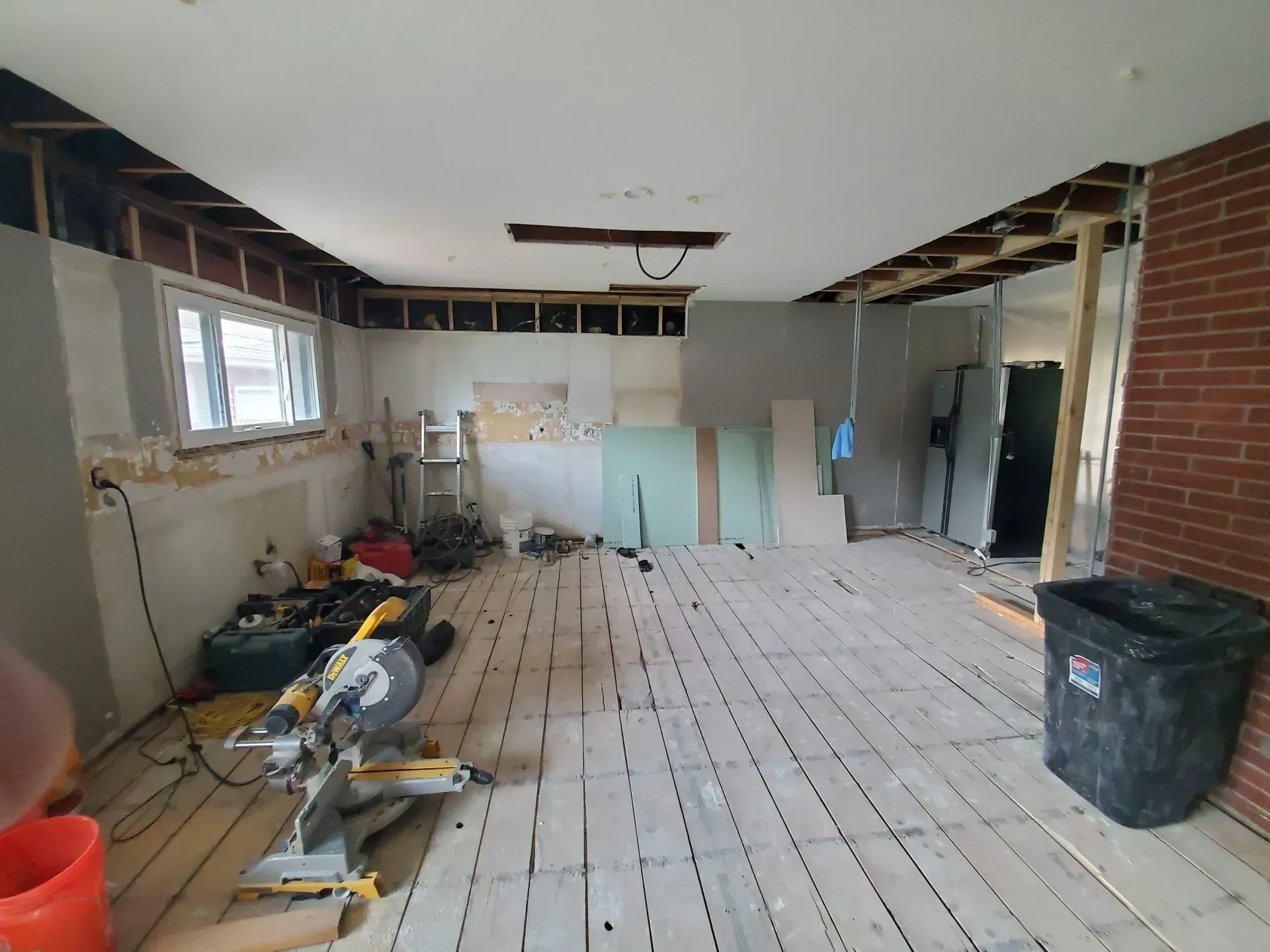 Room under renovation with exposed beams, wooden floor, and construction debris.