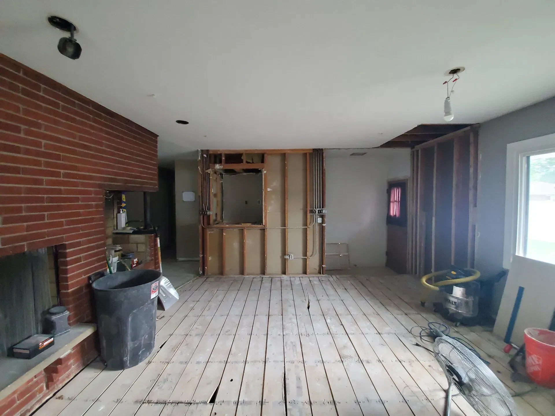 Interior room undergoing renovation; exposed wooden studs, brick fireplace, grey walls, and bare floorboards.
