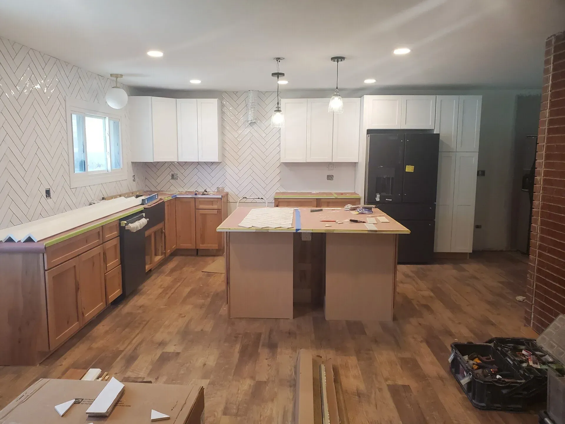 Kitchen under renovation with white and wood cabinets, island, new flooring, and tiled backsplash.