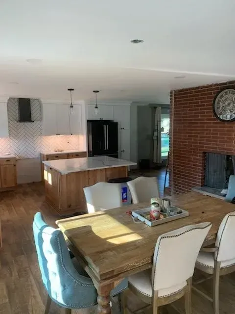 Open-concept kitchen and dining area with island, table, and brick fireplace. Light wood cabinets and floor.