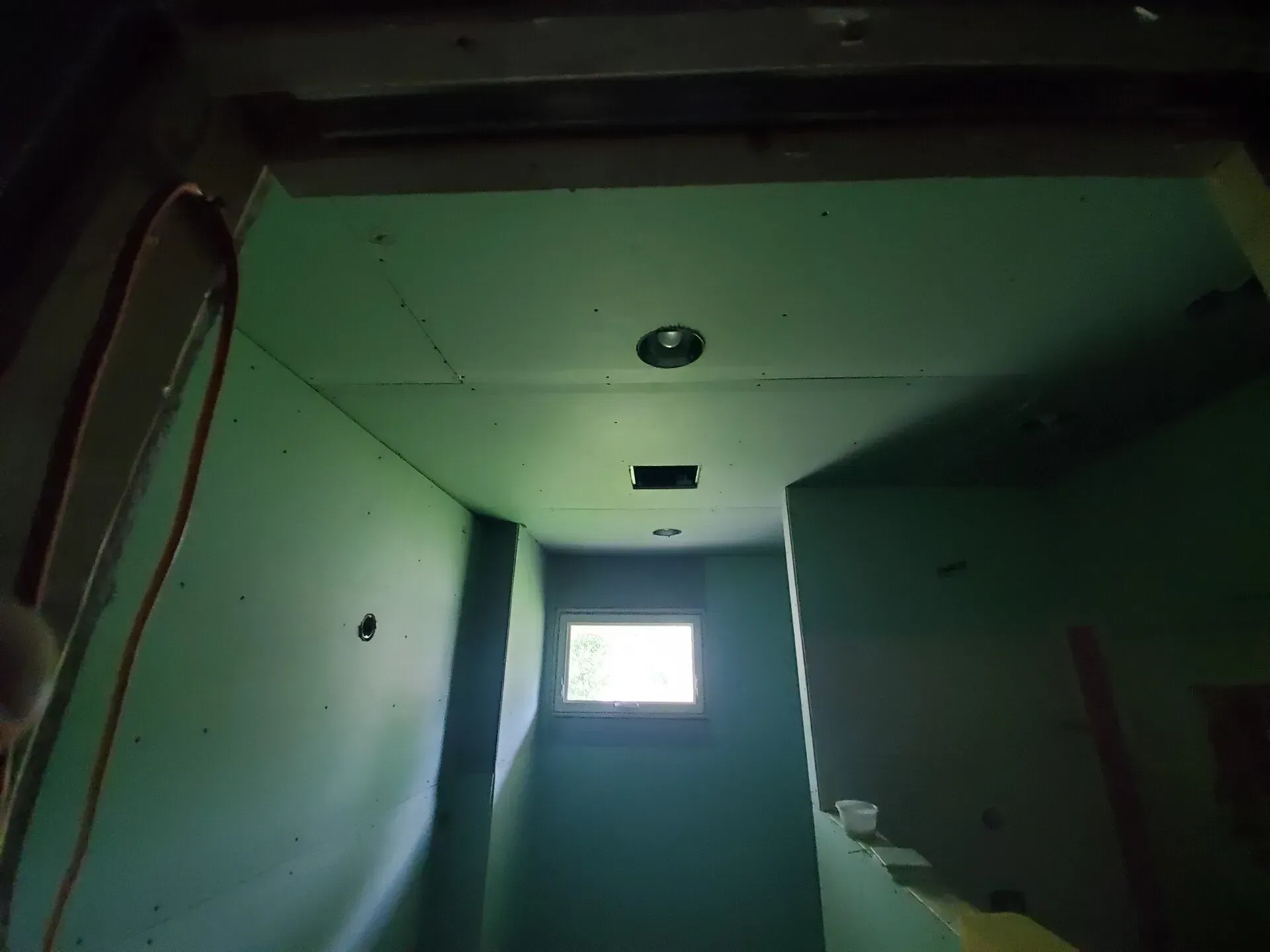 Interior view of a green-walled stairwell with a window at the end, ceiling light, and an open doorway.