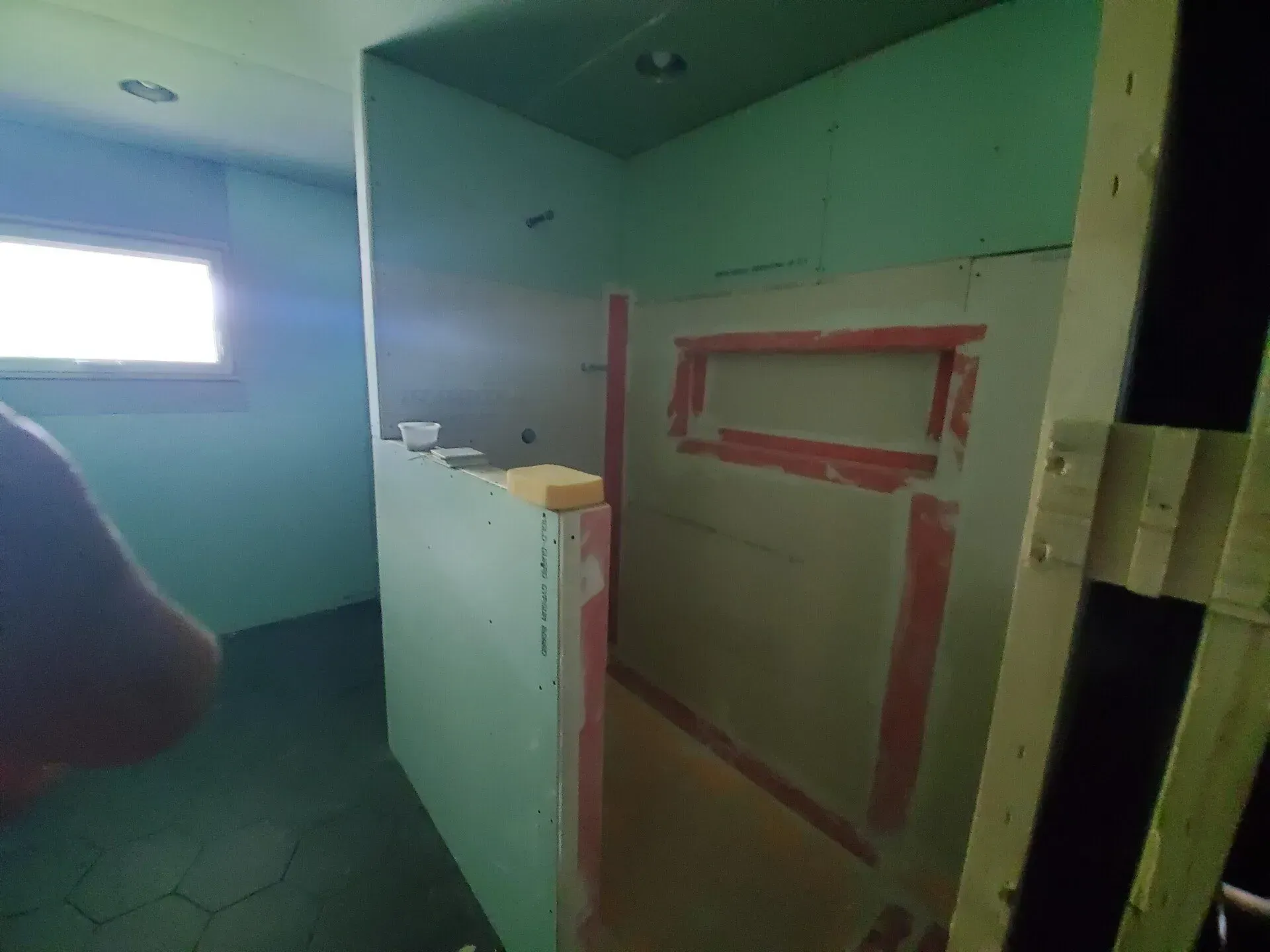 Bathroom under construction: green drywall, small window, shower alcove with a niche.