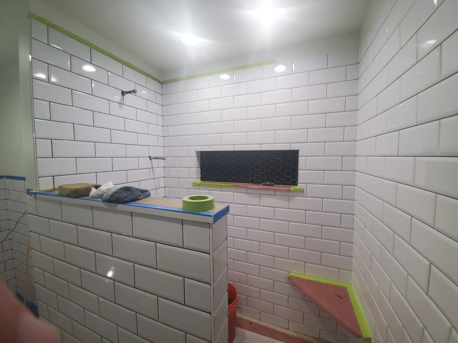 White tiled shower with a niche and showerhead, being renovated.