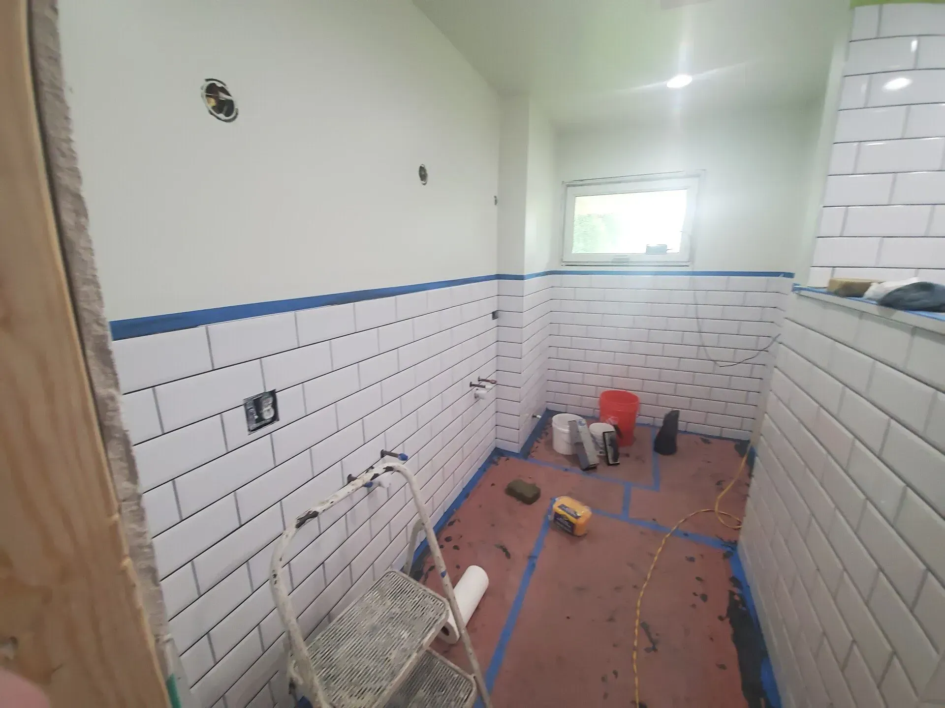 Bathroom under construction, white subway tile on walls, tools and ladder on floor.
