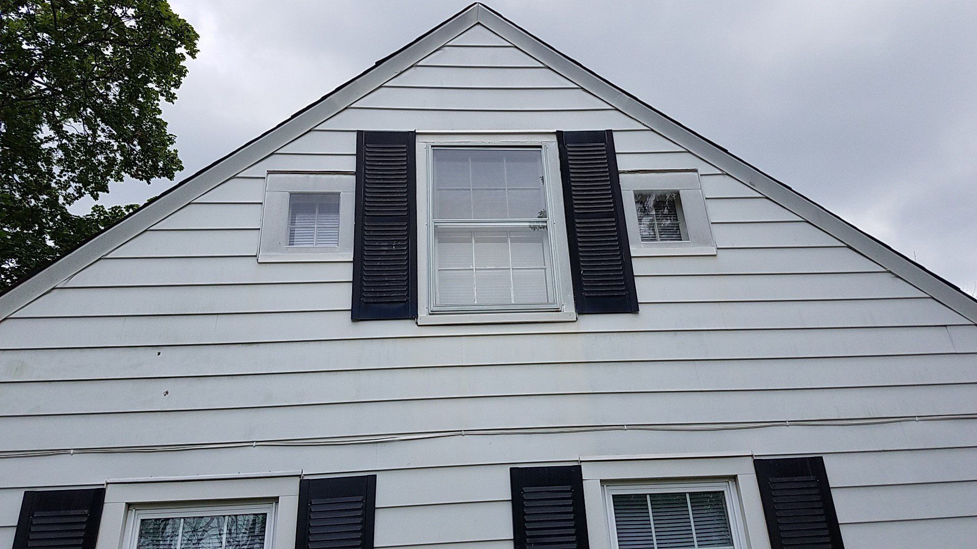 White house with black shutters, three windows on the upper portion, under a cloudy sky.