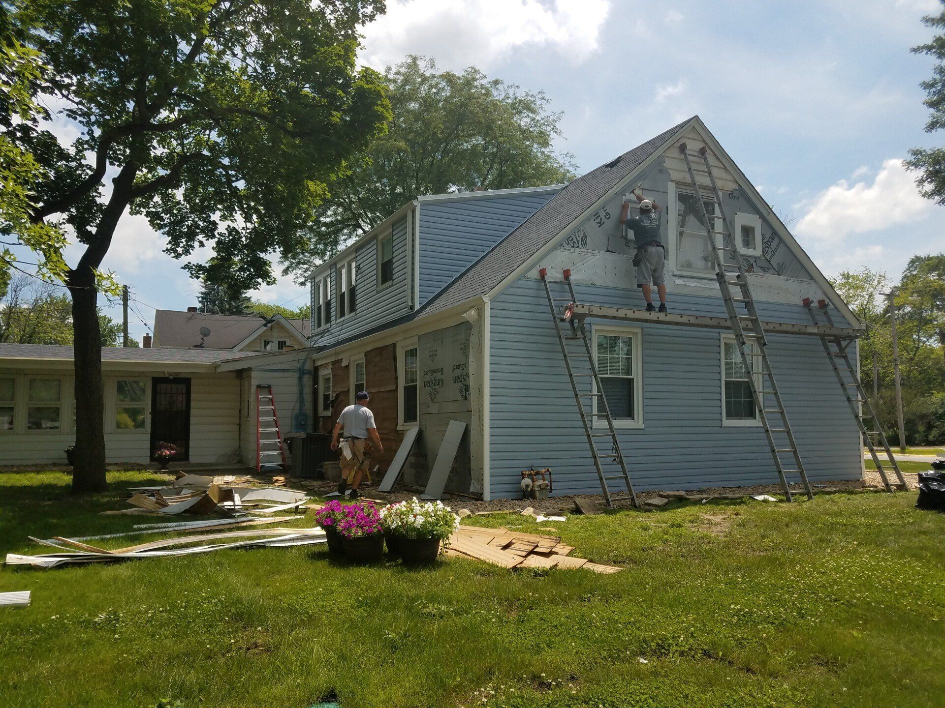 House with siding being replaced; workers on ladders. 