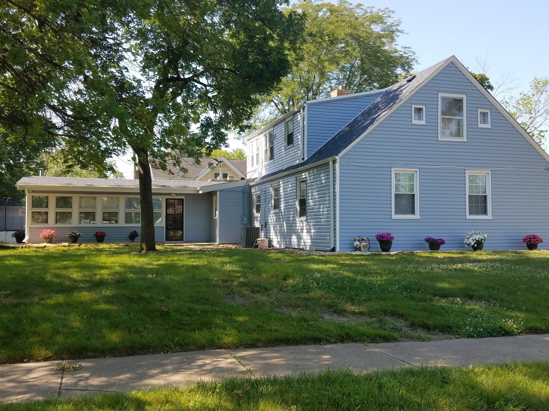 Blue house with a sunroom and a lawn, flowers in pots line the front.