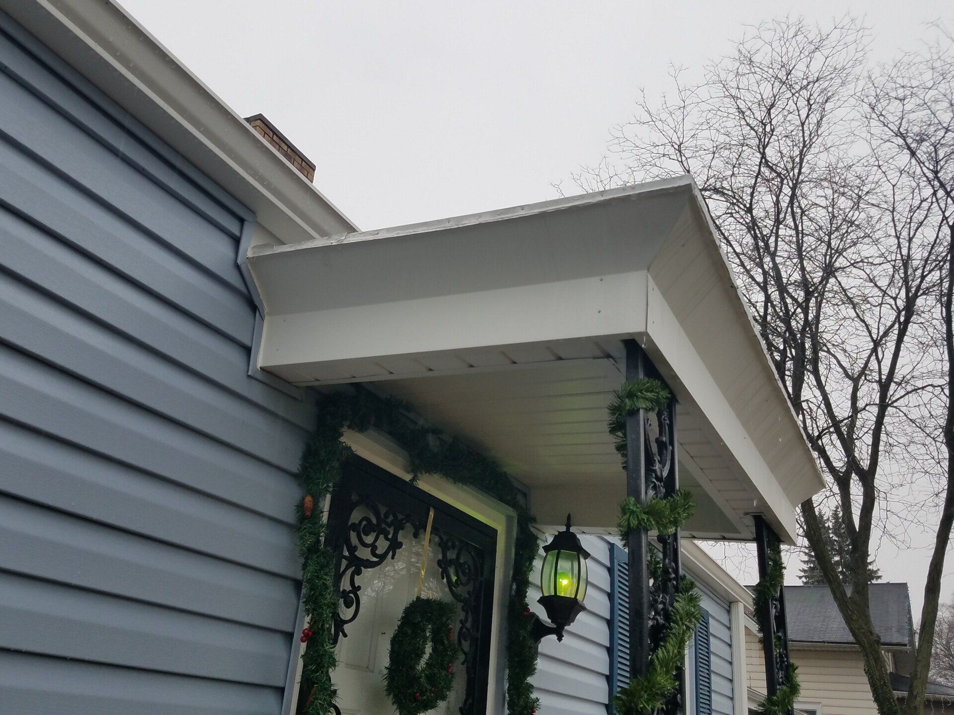 Blue house with white trim, Christmas decorations on the porch.