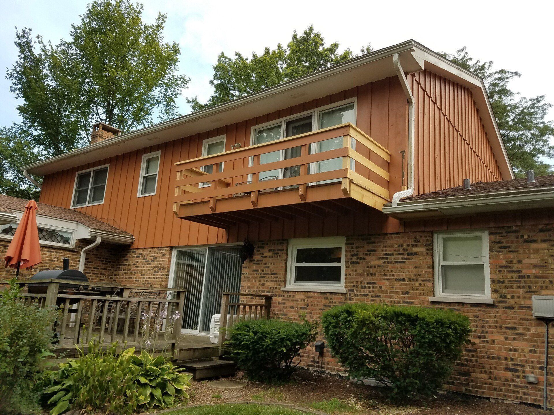 Back of a two-story brick and brown siding house with a deck.