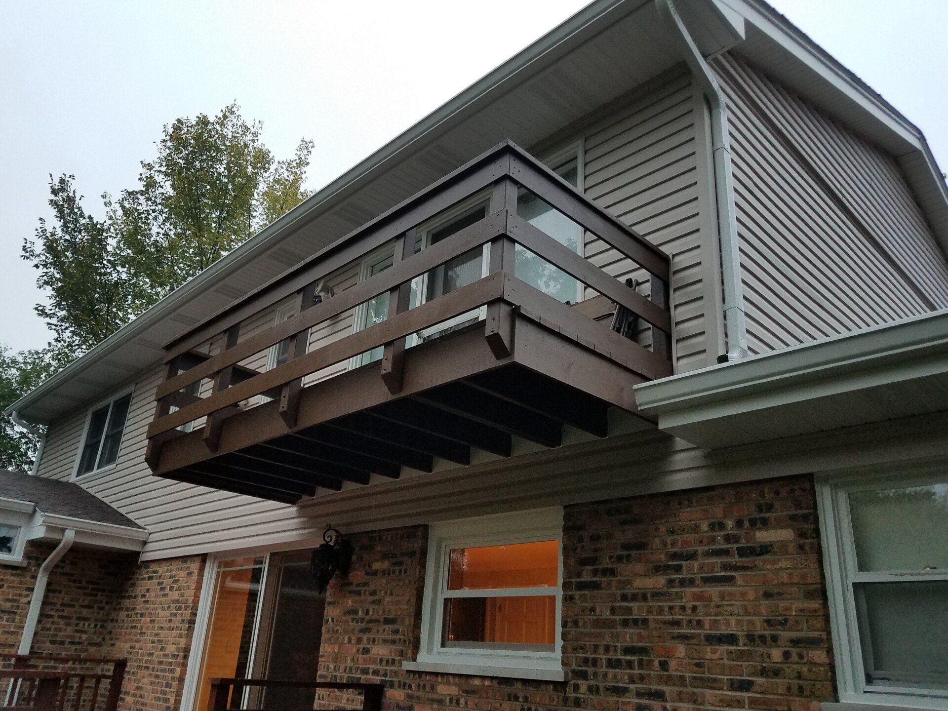 Brown elevated deck attached to a two-story beige house with a brick base.