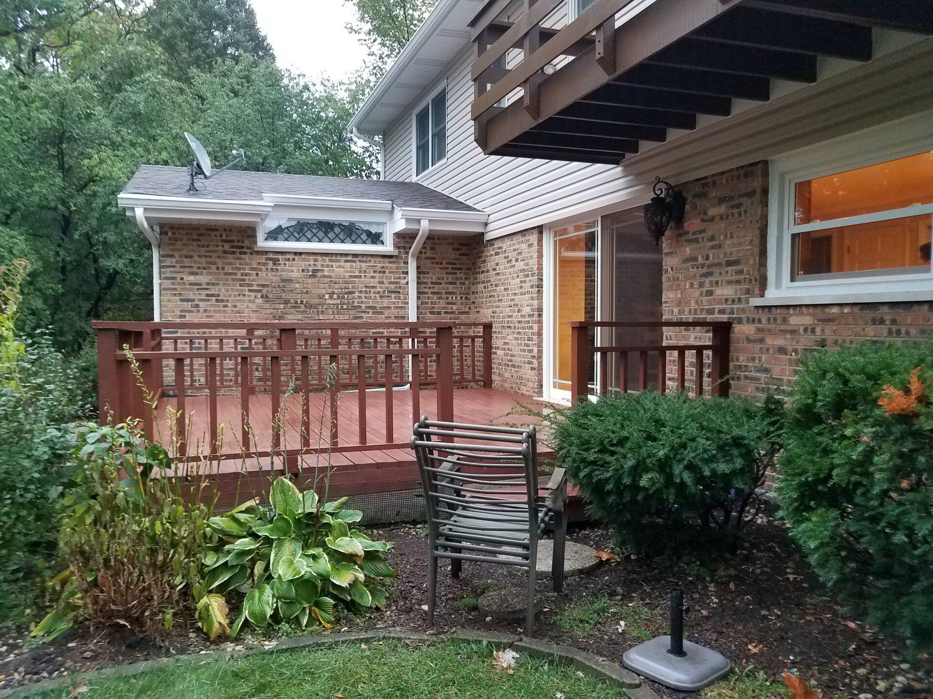Back of a two-story brick house with a wooden deck and a balcony.