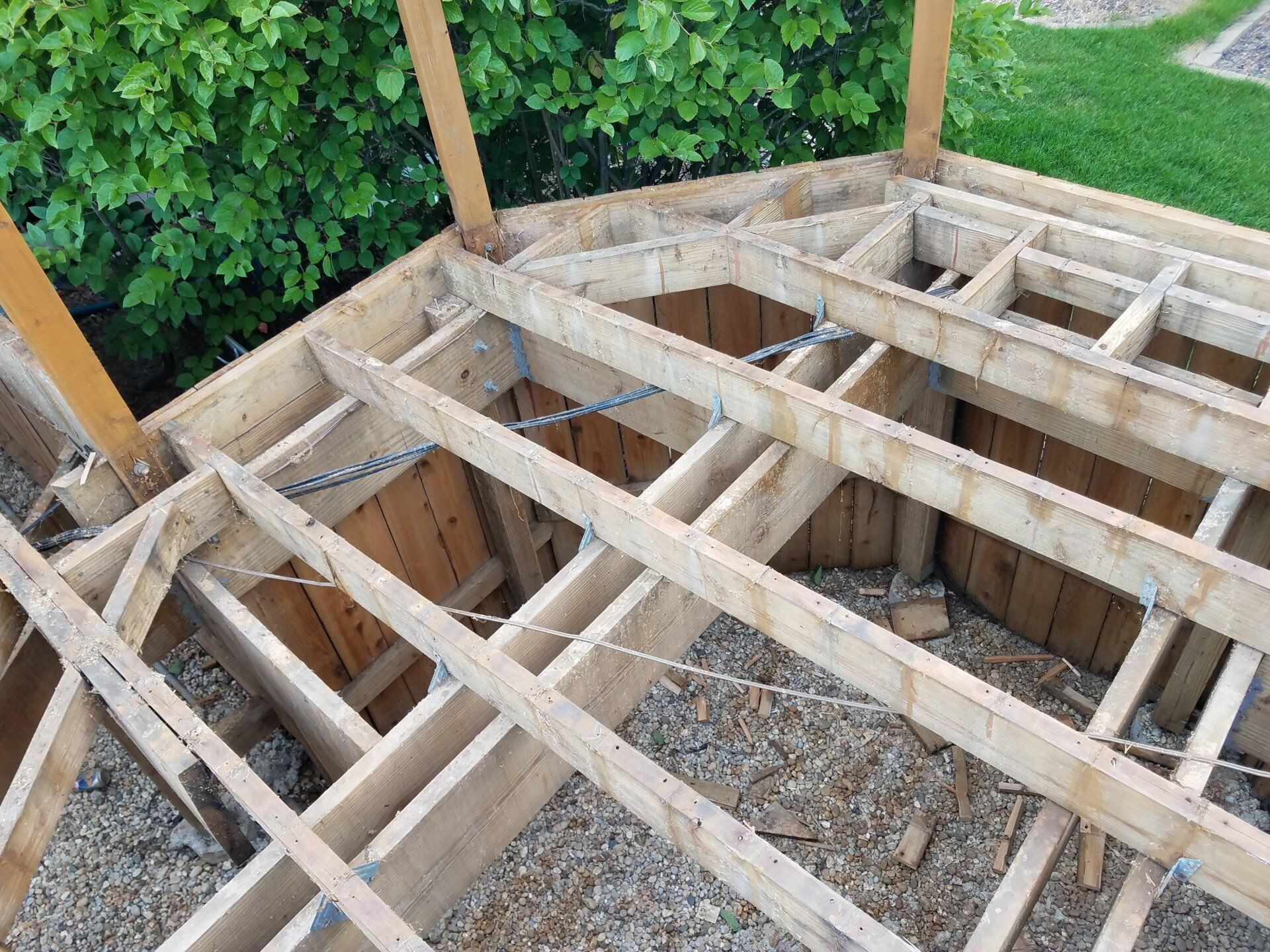 Wooden deck frame, partially constructed, with support beams and joists; outdoor setting.