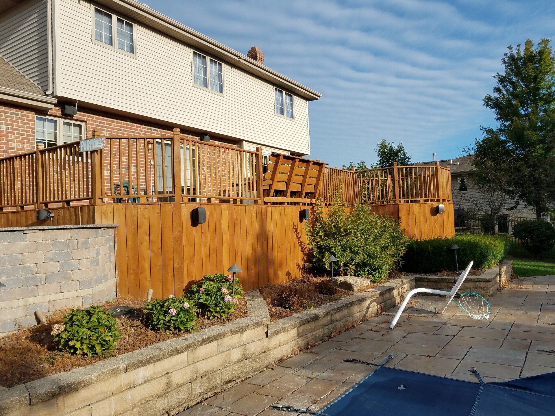 Wooden deck attached to a two-story house, overlooking a pool and landscaping.