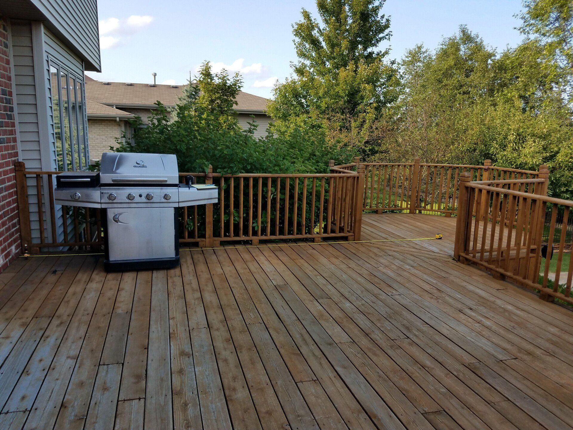 Wooden deck with a grill; brown railings and trees in the background.