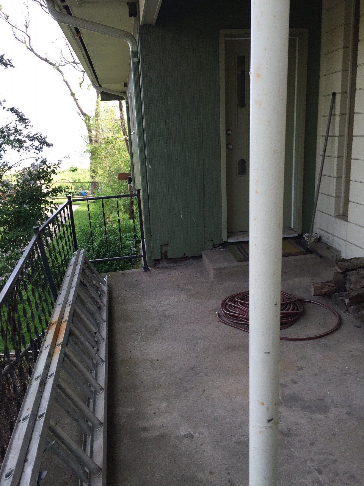 Exterior porch with concrete floor, green siding, and a white pillar. 