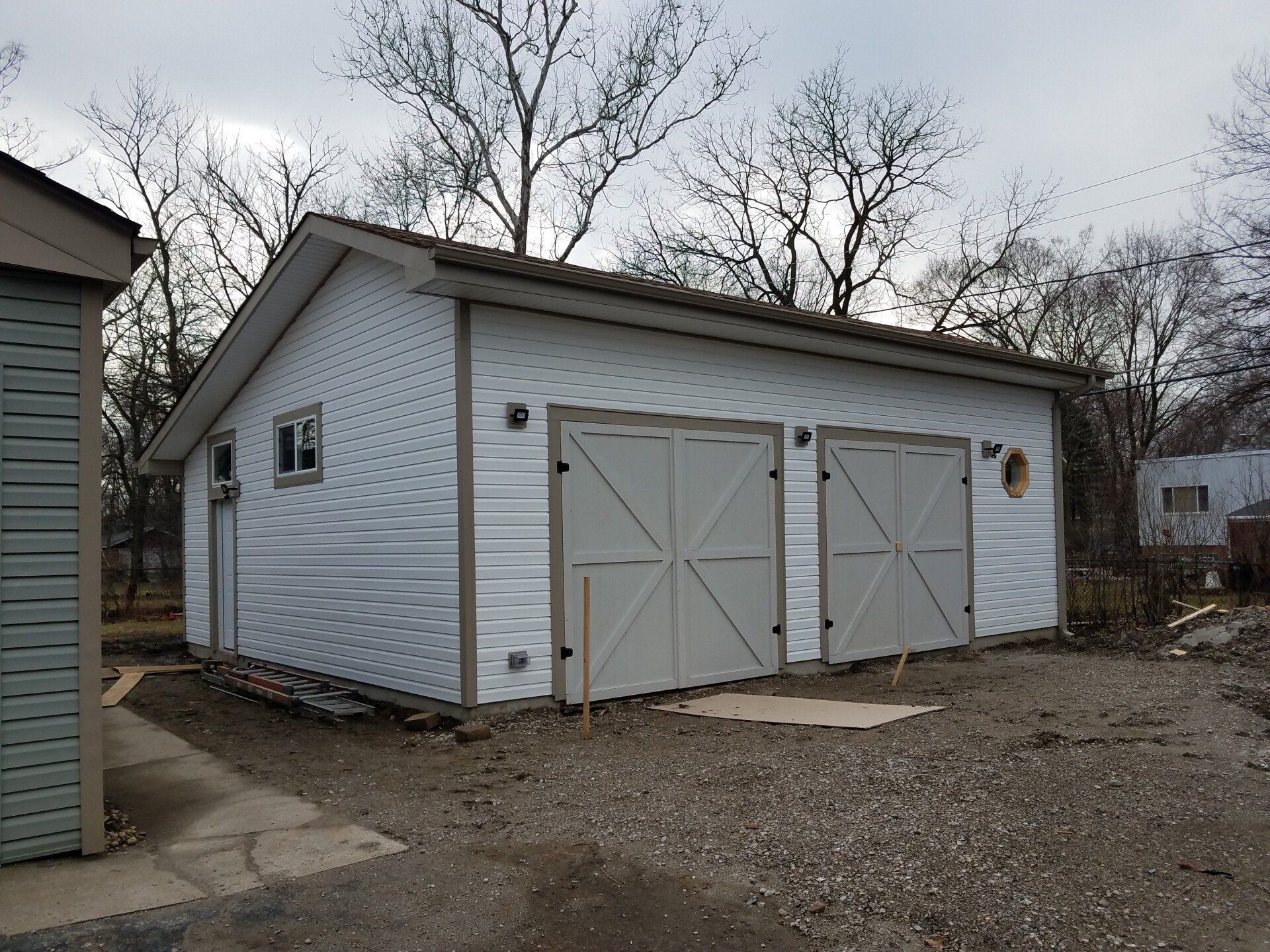 White garage with two gray doors, window, and brown trim, gravel driveway.