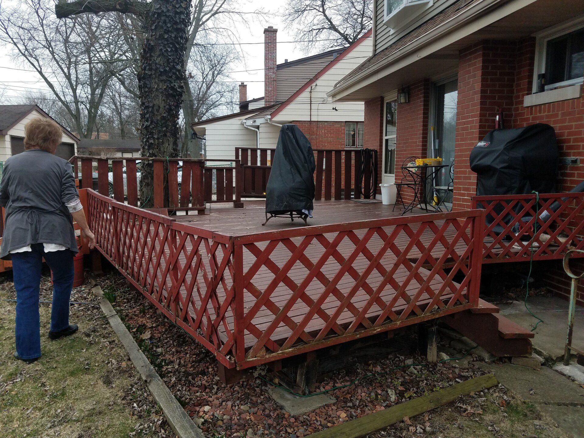 Person walking towards a red wooden deck, attached to a brick house, under an overcast sky.