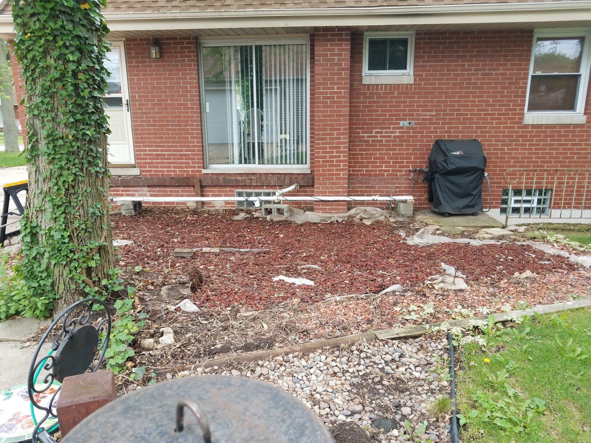 Backyard with brick house, mulch ground cover, covered grill, tree with ivy, and a sliding door.