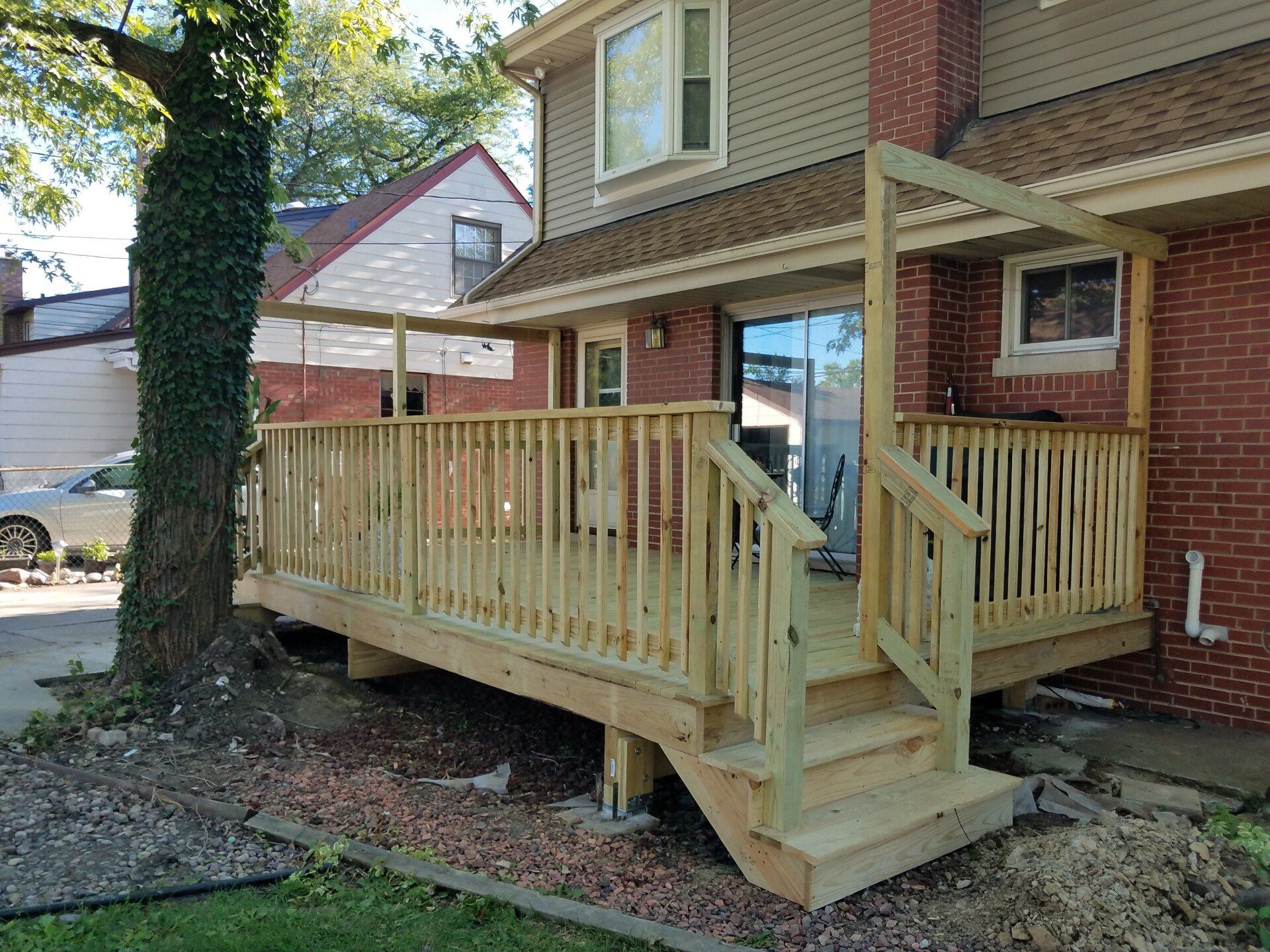 Wooden deck with stairs, railing, and a covered section attached to a brick house.