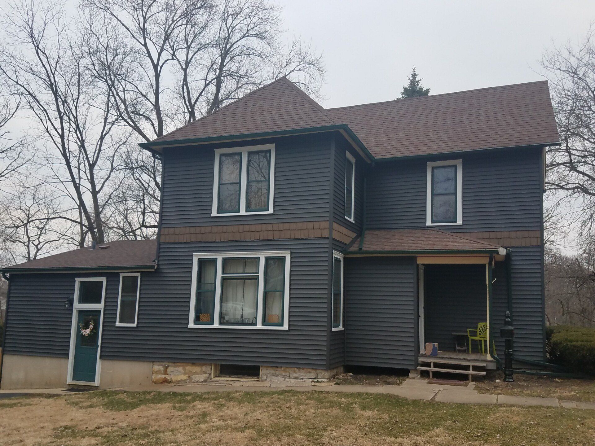 Two-story house with dark gray siding, brown roof, and small porch. 
