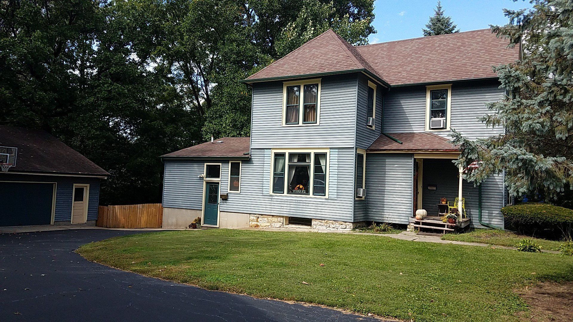 Two-story house with detached garage, blue siding, brown roof, and driveway on a grassy lawn.