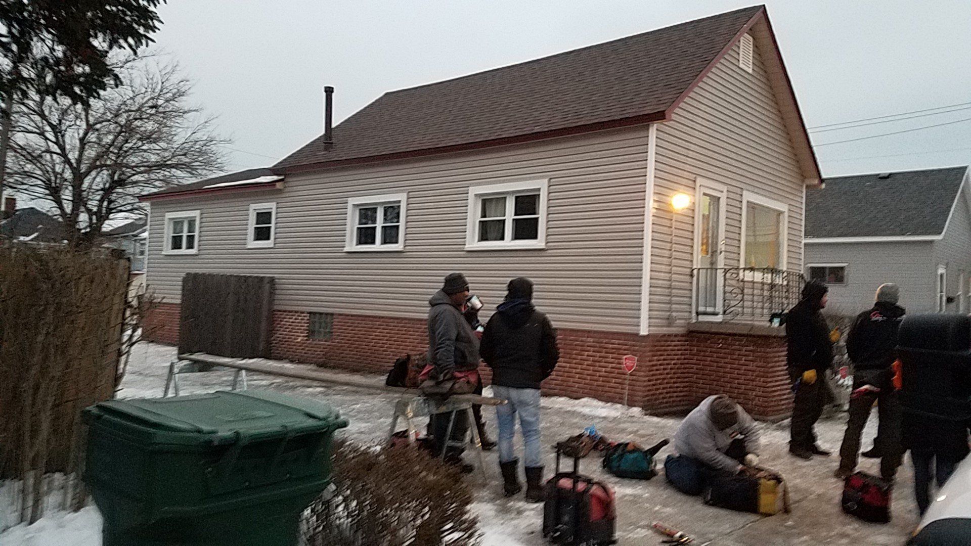 House exterior with workers, tools, and snow, overcast day.