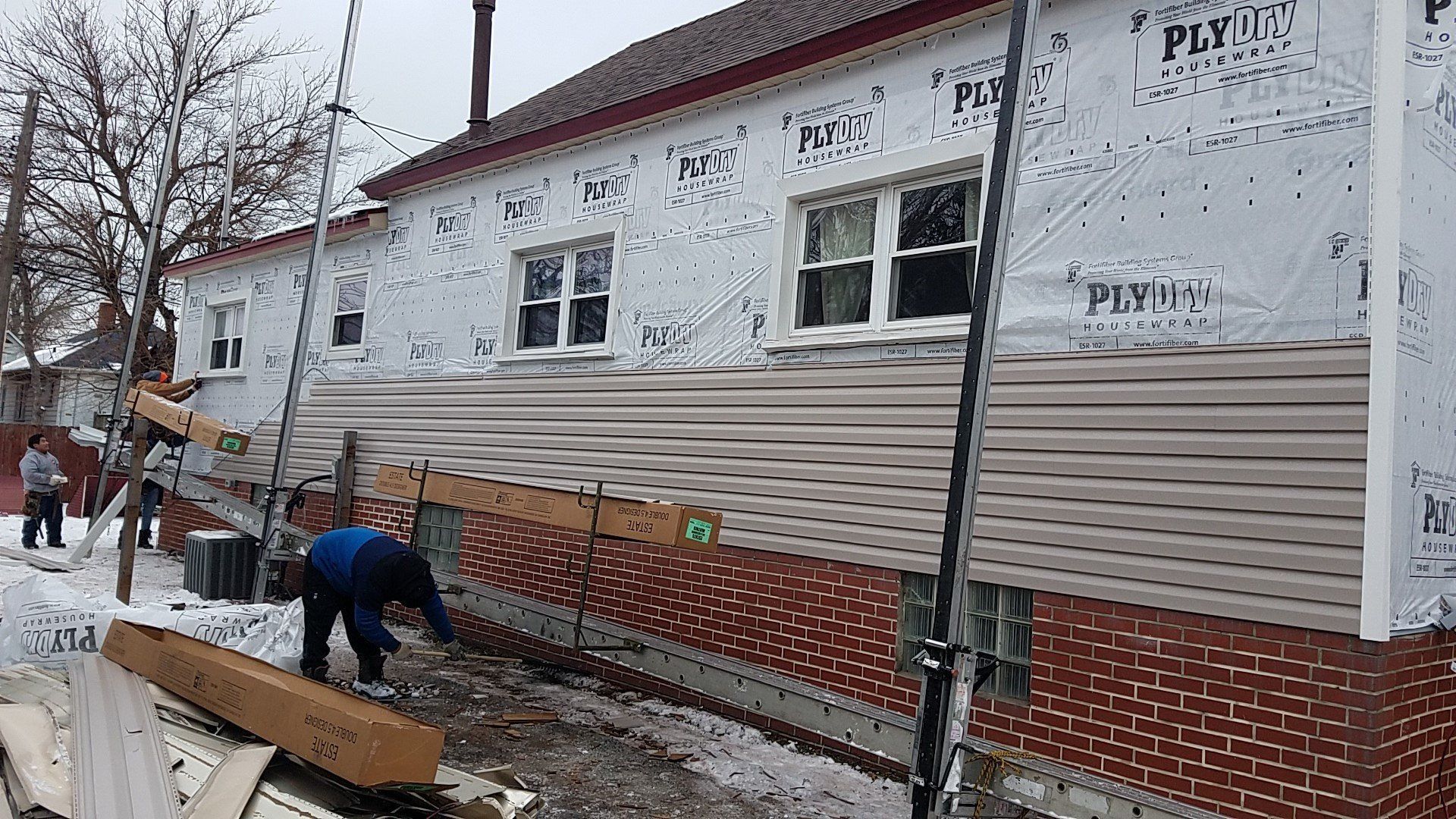 Workers installing siding on a brick building with windows, winter setting.