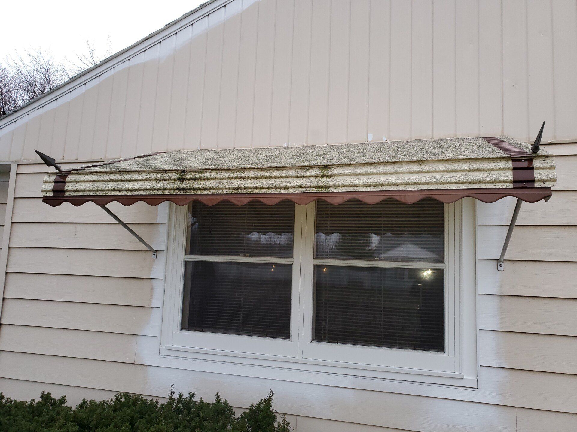 Weathered awning above a window on a light-colored house. 