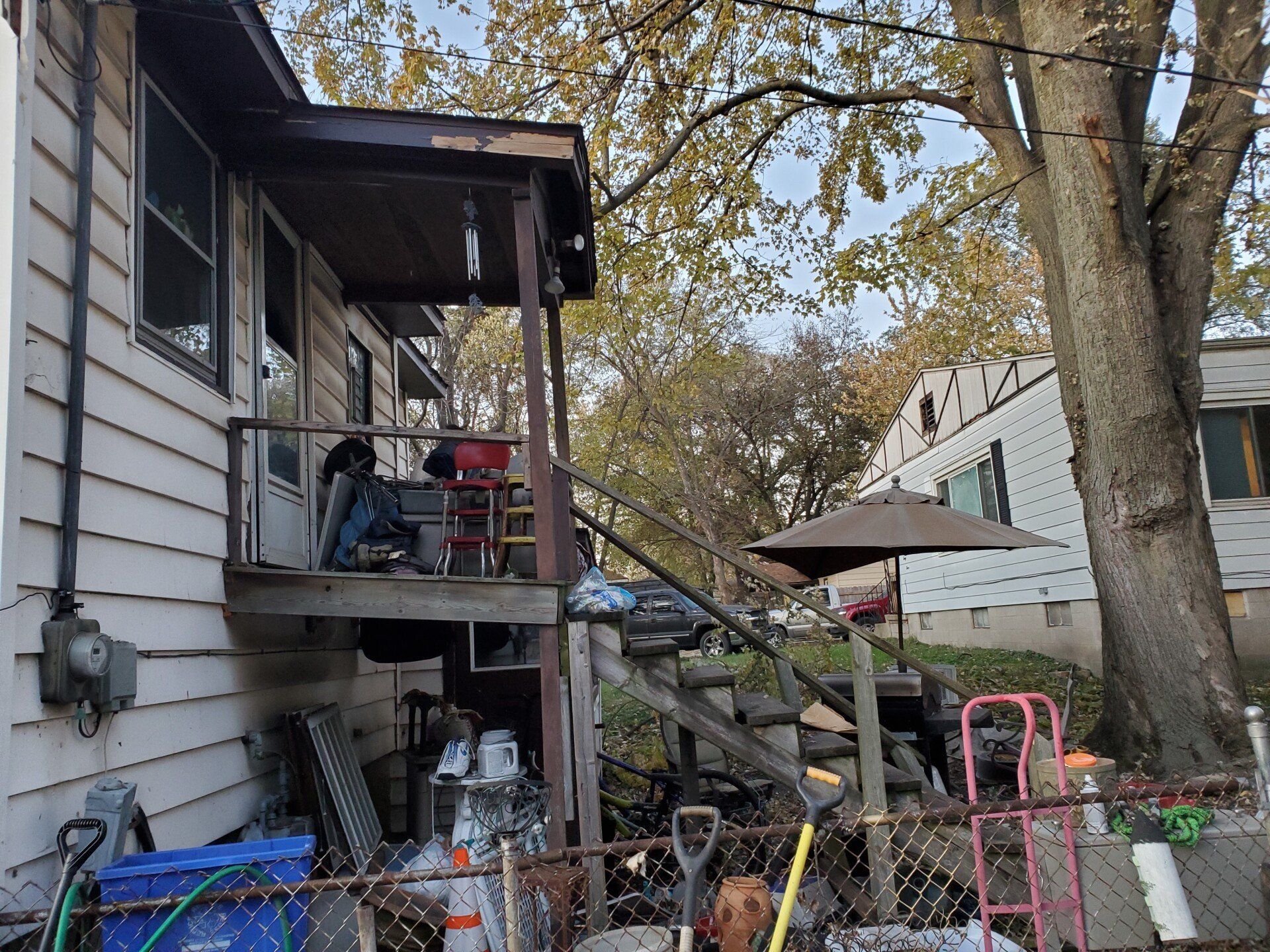 Side view of a weathered house with a porch and cluttered stairs. 
