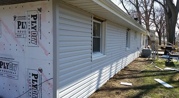 House exterior with white siding being installed, featuring windows and a partially covered corner.