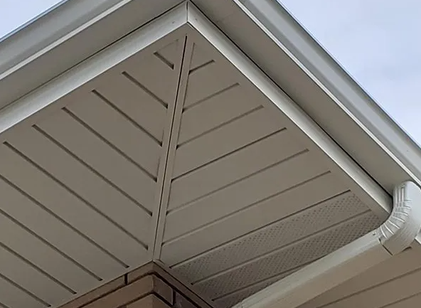White soffit and trim on a building's corner with angled, grooved panels and a gutter.