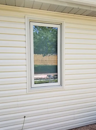 White siding with a rectangular window, partially open, reflecting trees and a fence.