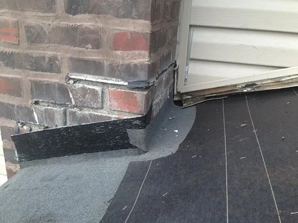 Brick chimney with flashing against siding and flat roof.