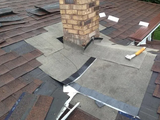 Roof under repair near a brick chimney with exposed underlayment and flashing.
