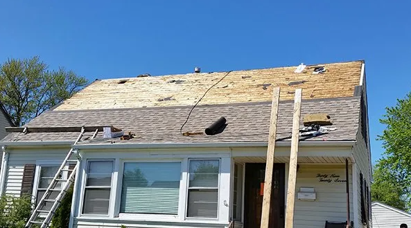 House with roof partially stripped during repair, blue sky background. Wooden ladders and supports visible.
