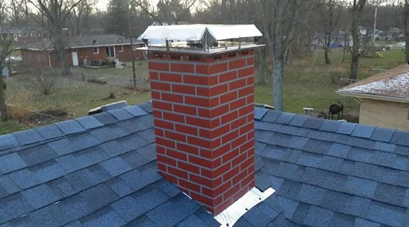 Brick chimney with a metal cap atop a dark gray shingled roof.