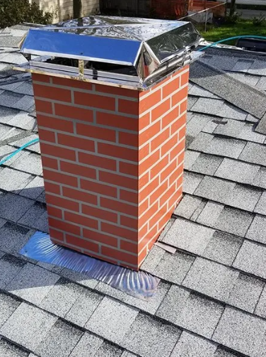 Brick chimney on a gray shingled roof, with a metal cap.
