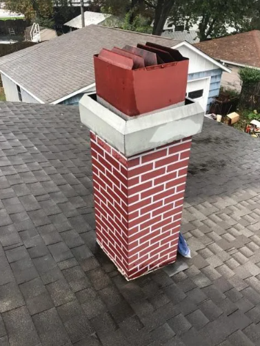 Brick chimney with a red metal cap and silver trim on a shingle roof.