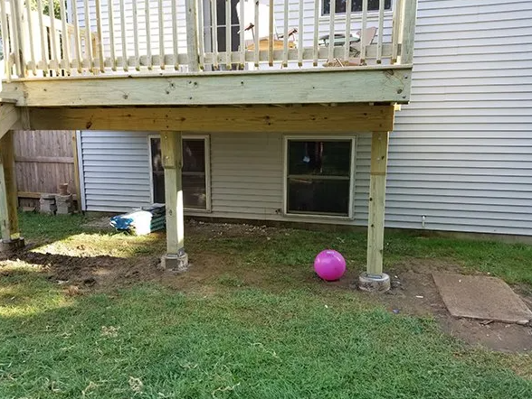 Deck supported by wooden posts and concrete blocks; pink ball on grass.
