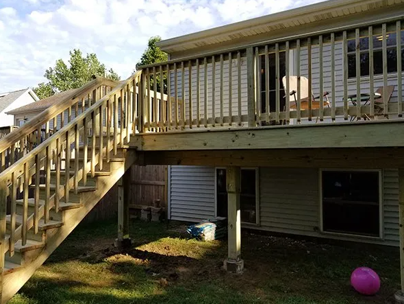 Wooden deck with stairs leading to a house with siding; cloudy sky.