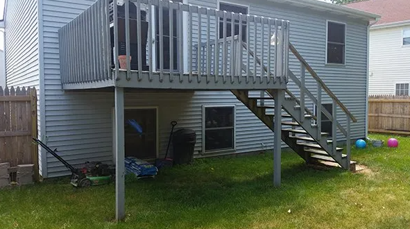 Backyard deck with stairs leading down to a grassy yard. Gray siding, wooden fence.