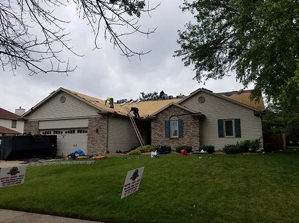 Roofers working on a residential home with exposed roof structure; green lawn, cloudy sky.