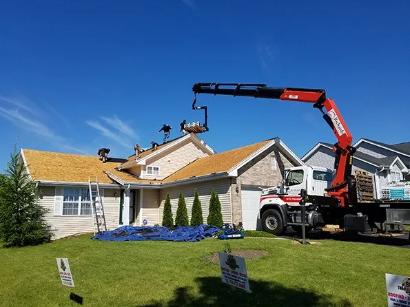 Roof replacement in progress: Crane lifting equipment to a house roof on a sunny day.