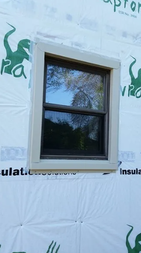 Window framed in tan trim on a building covered in white and green protective material.