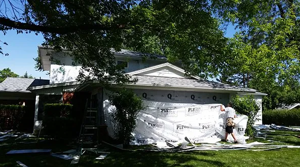 House being wrapped in Tyvek. A worker is installing the protective barrier on the exterior of the house.