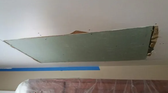 Hole in a ceiling with exposed drywall. Blue tape on wall below.
