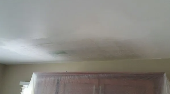 Water damage on a white ceiling, above a covered brown cabinet.