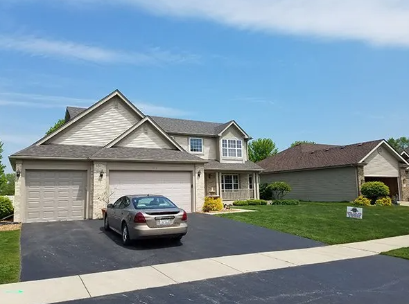 House with tan siding, three-car garage, and car in driveway, green lawn, and blue sky.